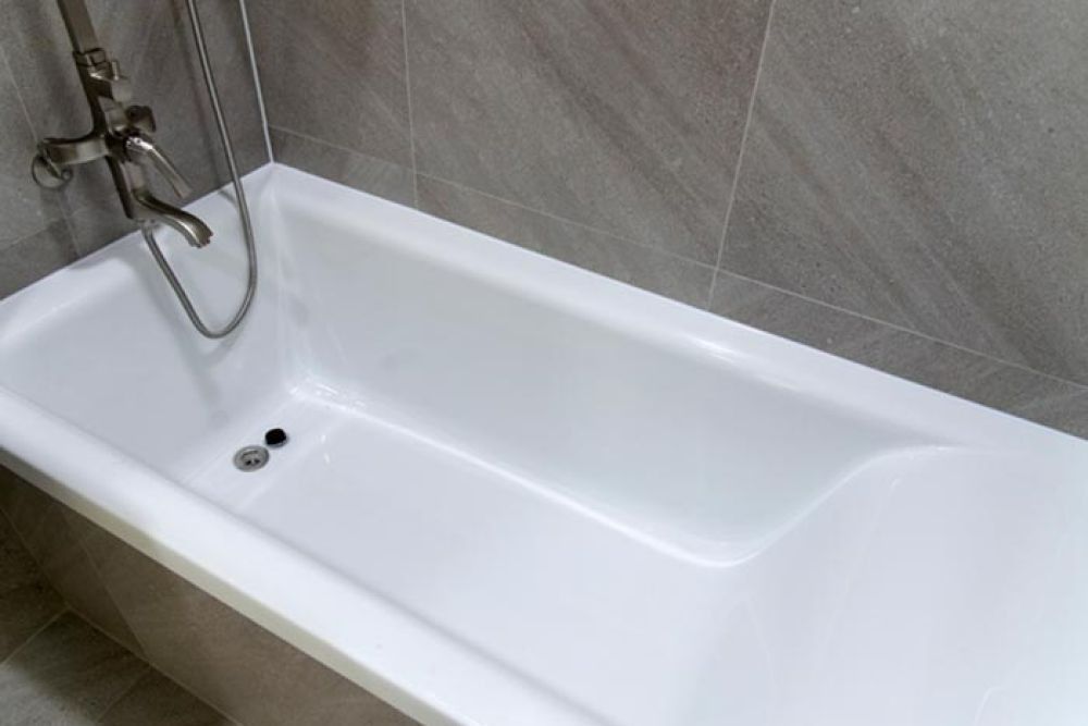 White bathtub with a chrome faucet against gray tiled wall.