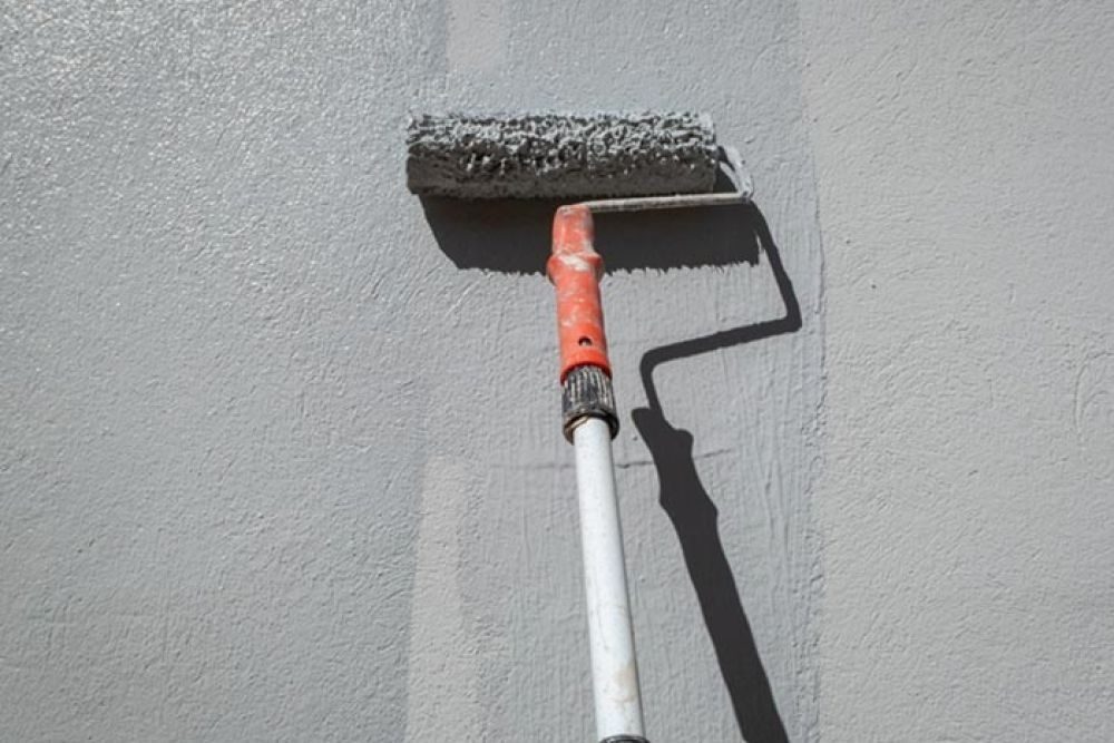 Paint roller on a wall, painting gray.