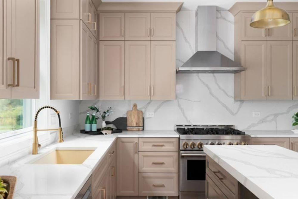 Beige kitchen with marble countertops, stainless steel range hood, gold hardware.