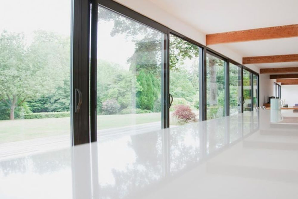 Long hallway with large windows overlooking a green yard, white floor reflects light.