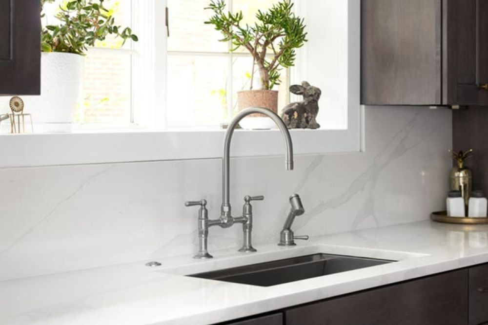 Stainless steel kitchen faucet over a dark sink, against a white countertop and window.