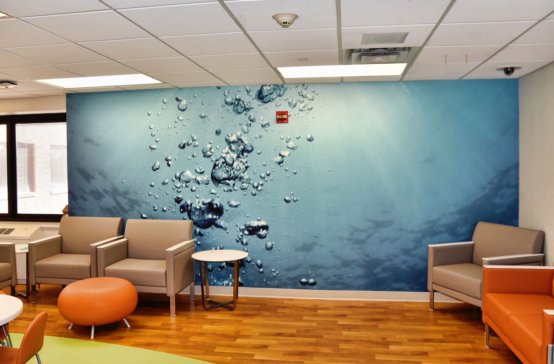 A waiting room with chairs and orange furniture against a large, aquatic-themed wall mural of underwater air bubbles.