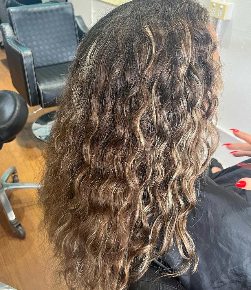 A Woman With Long Curly Hair is Sitting in a Chair in a Salon — Hairenvy in Ettalong Beach, NSW