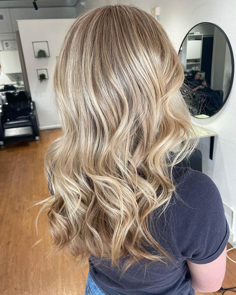A Woman With Blonde Hair is Standing in Front of a Mirror in a Salon — Hairenvy in Ettalong Beach, NSW
