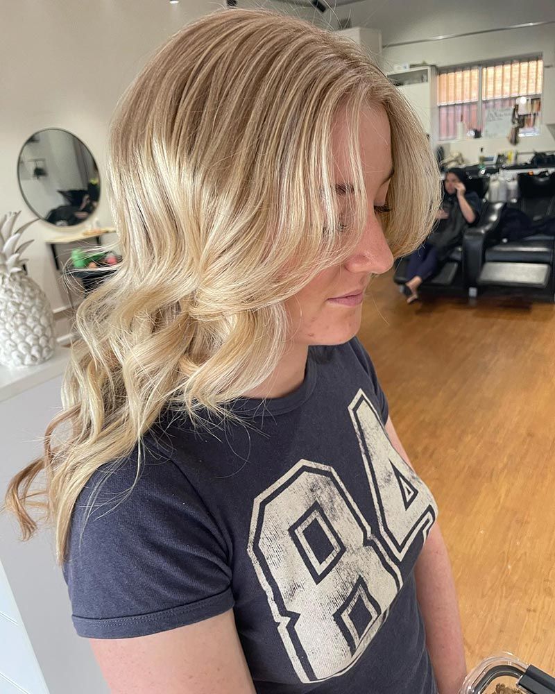A Woman With Blonde Hair is Wearing a Blue Shirt With the Number 84 on It — Hairenvy in Ettalong Beach, NSW