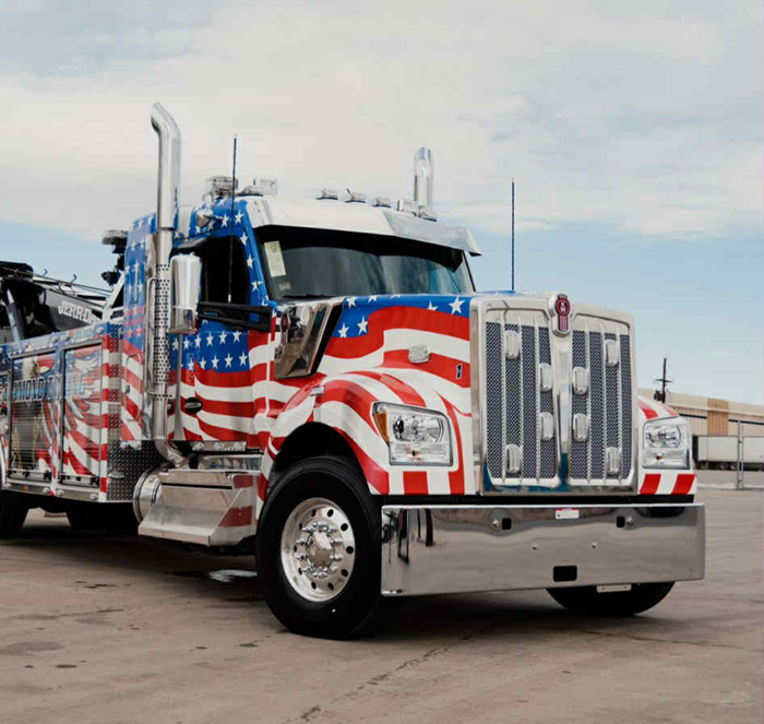 American flag-themed tow truck parked outside. Truck features a red, white, and blue design.