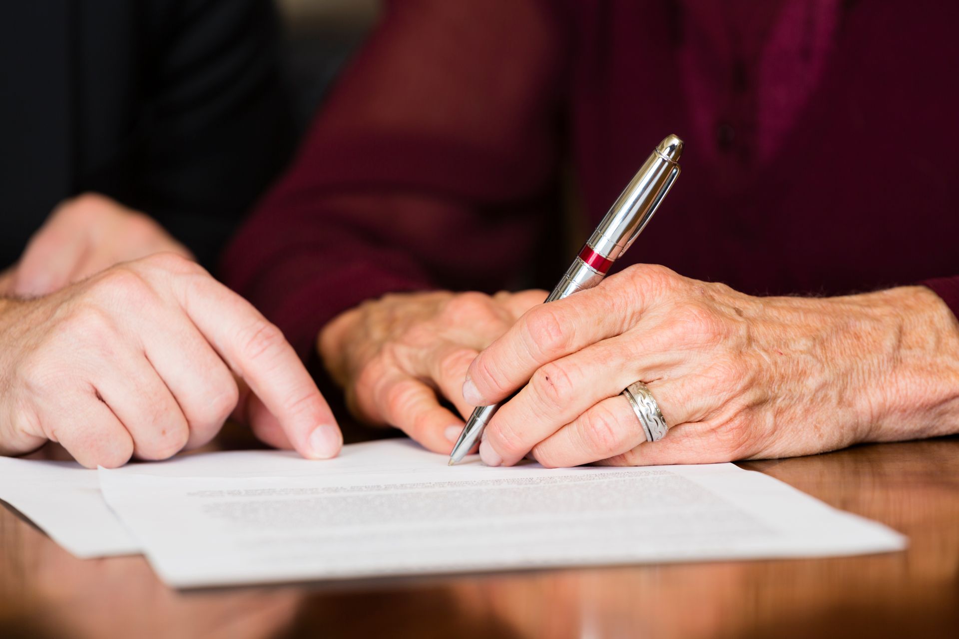 An elderly woman is signing a document with a pen.