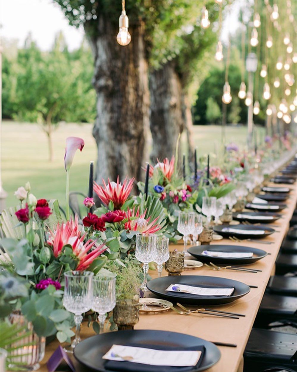 Un lungo tavolo con sopra piatti, bicchieri e fiori.