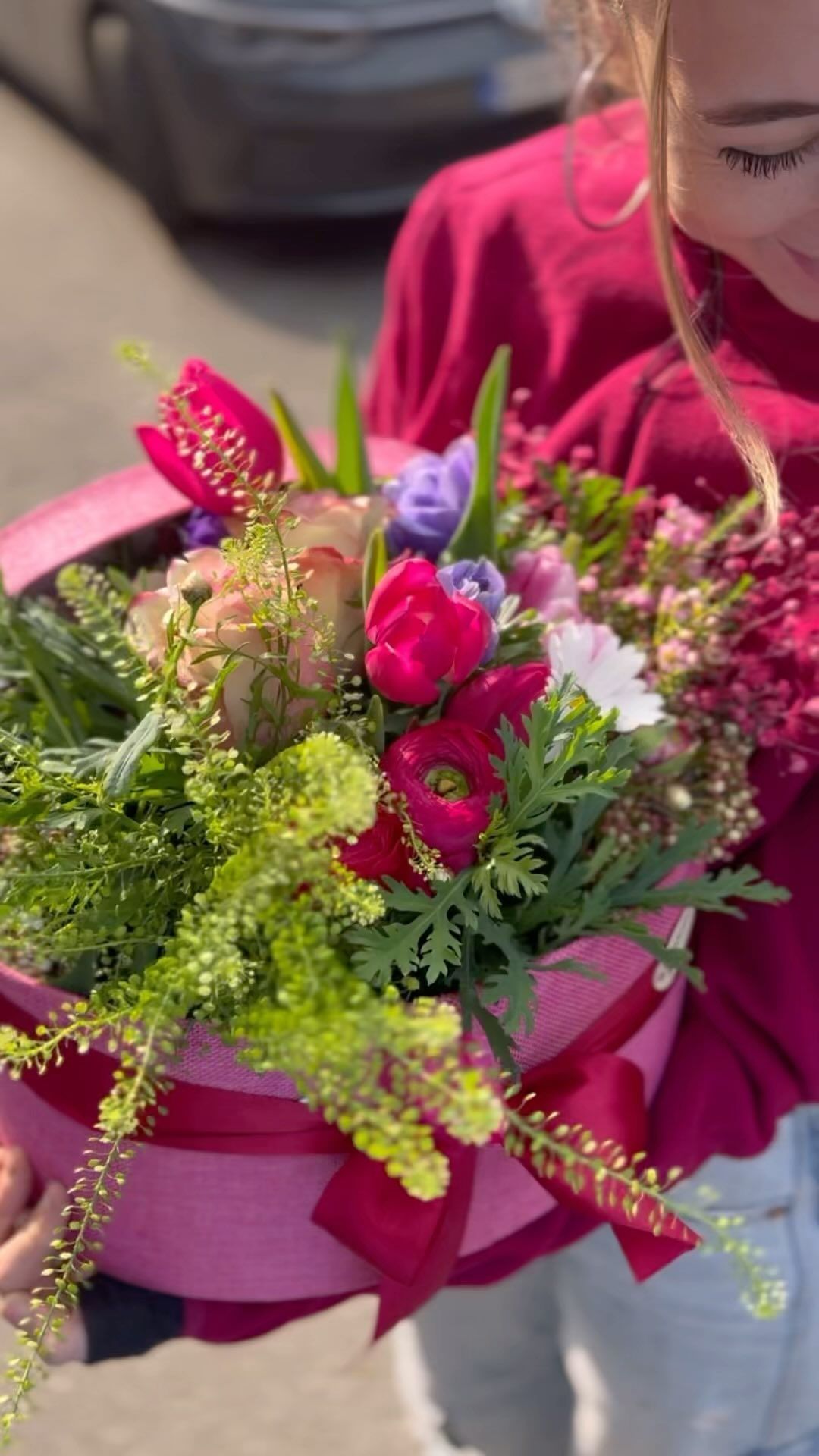 Una donna tiene in mano una scatola rosa piena di fiori.