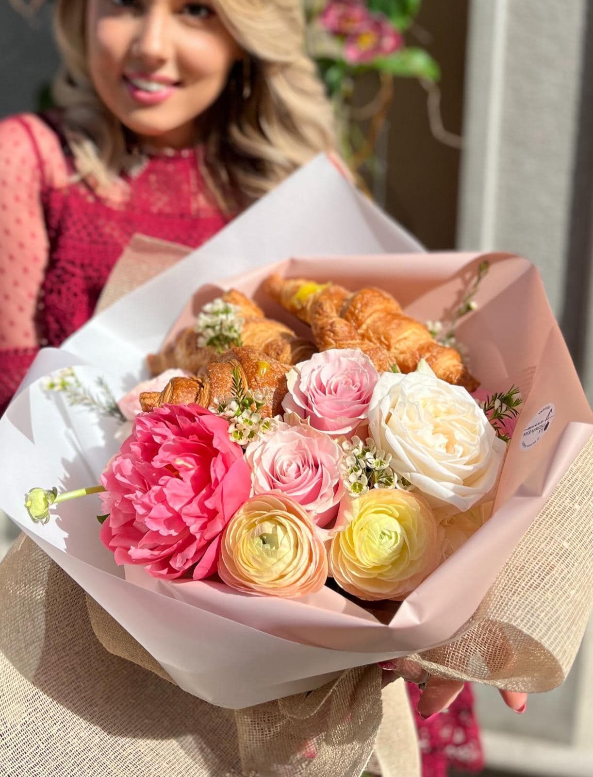 Una donna tiene in mano un mazzo di fiori e croissant.