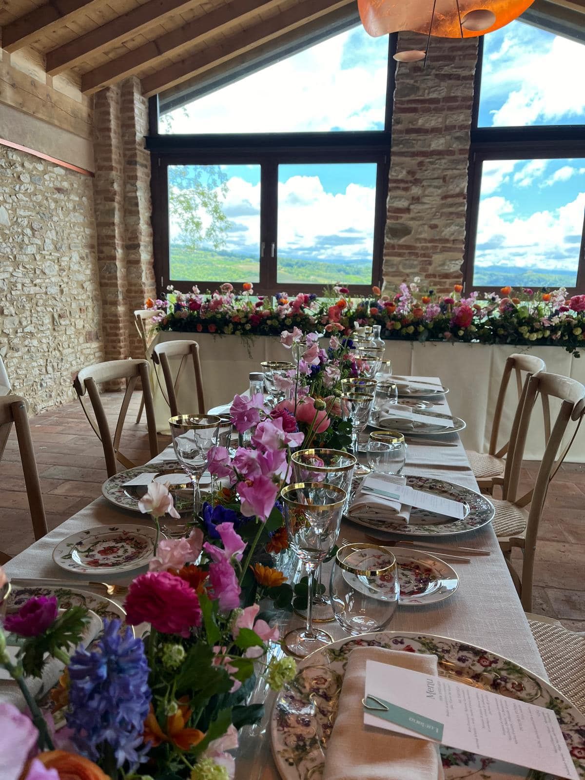 Un lungo tavolo con sopra piatti, bicchieri e fiori.