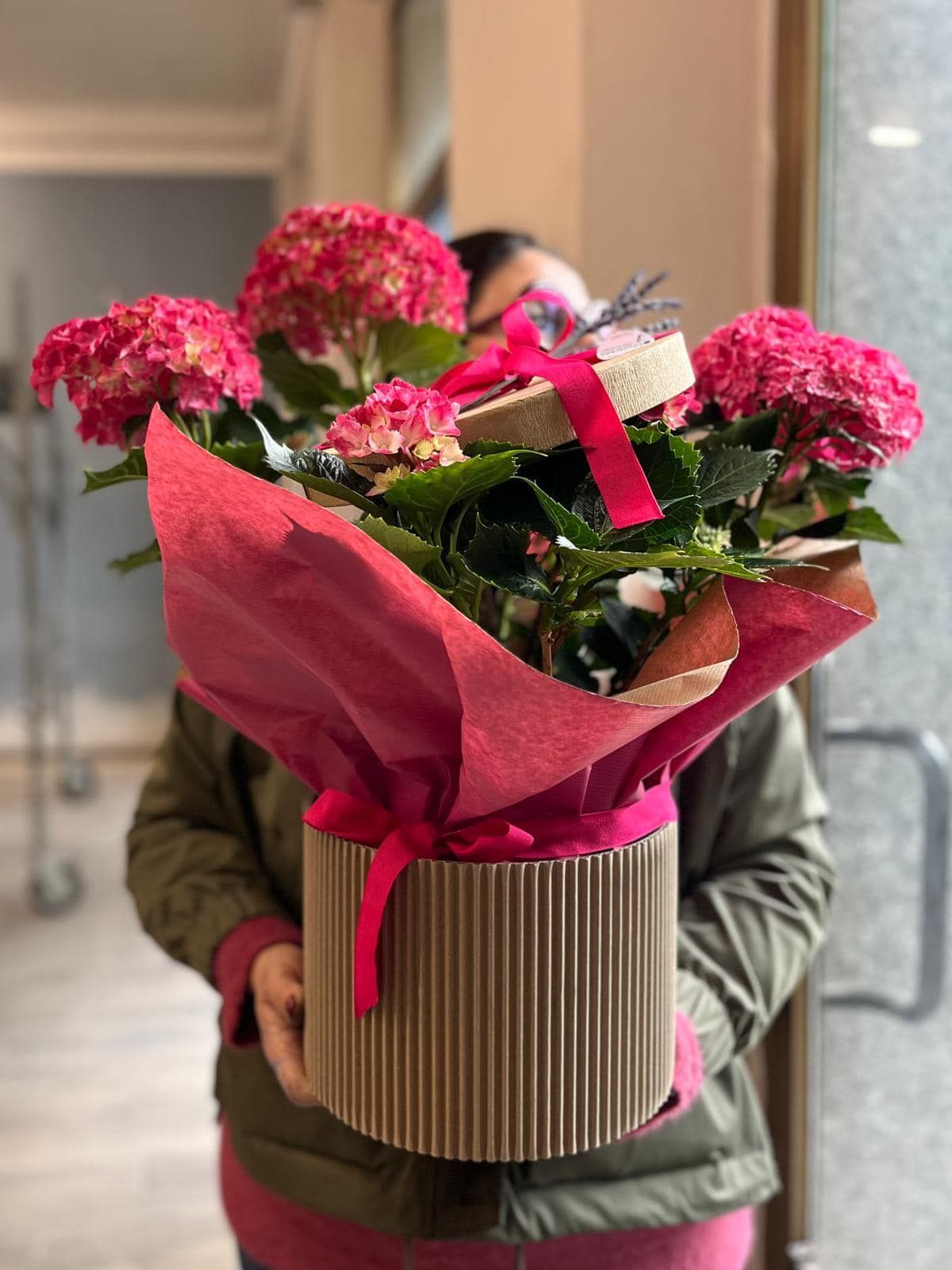 Una donna tiene in mano una scatola di cartone piena di fiori rosa.