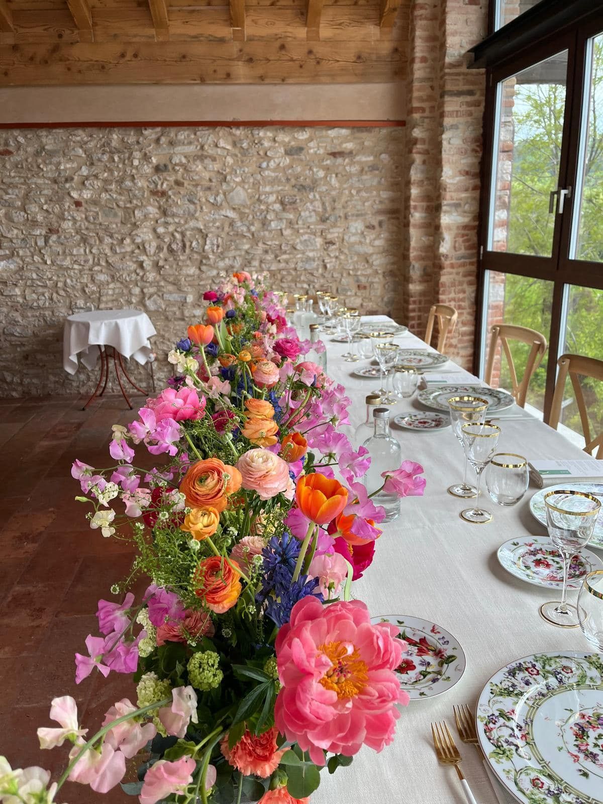 Un lungo tavolo con sopra piatti, bicchieri e fiori.