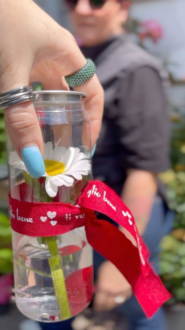 Una persona tiene in mano una lattina trasparente con dentro un fiore