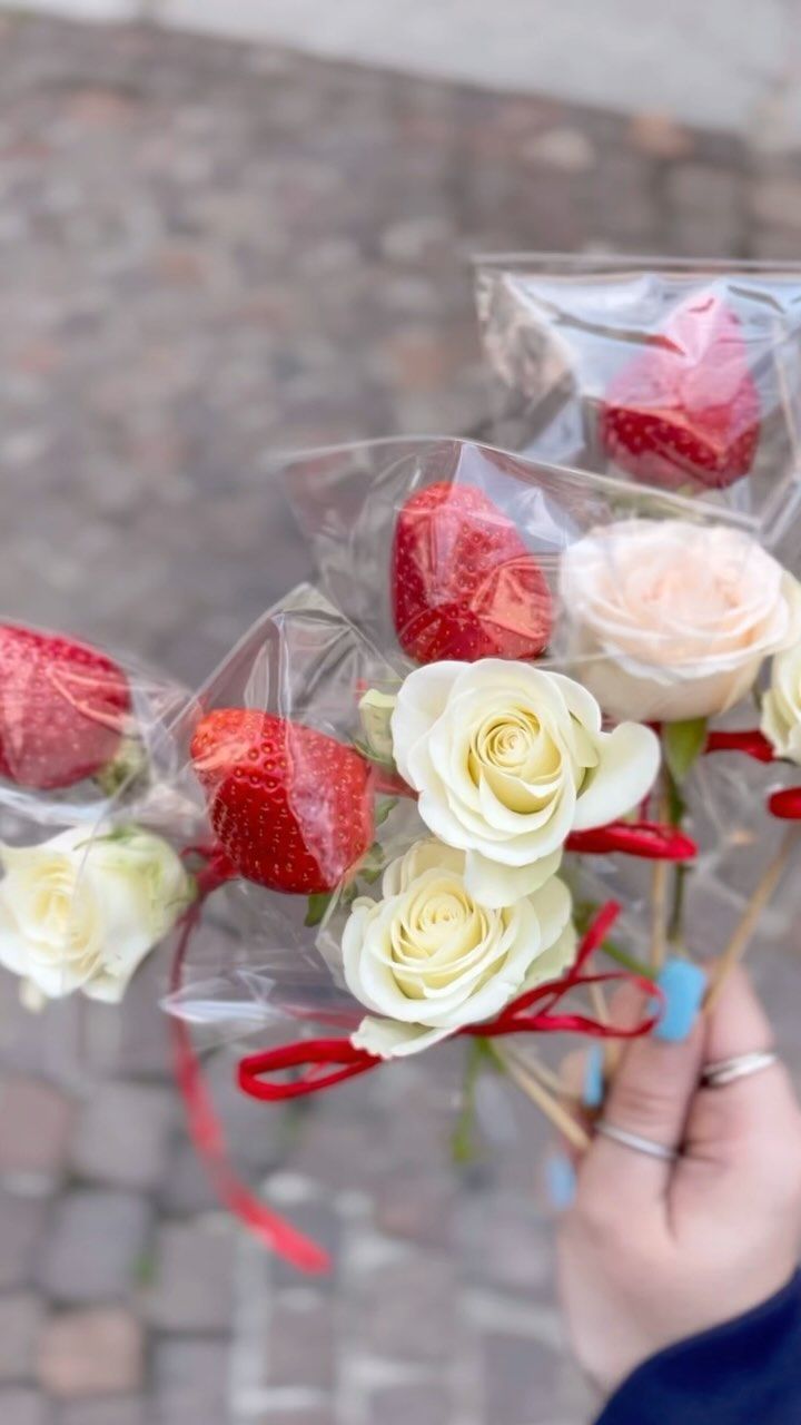 Una persona tiene in mano un mazzo di rose e fragole avvolte nella plastica.