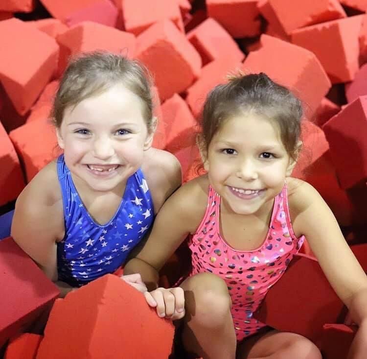 Two little girls are sitting in a pile of red foam cubes