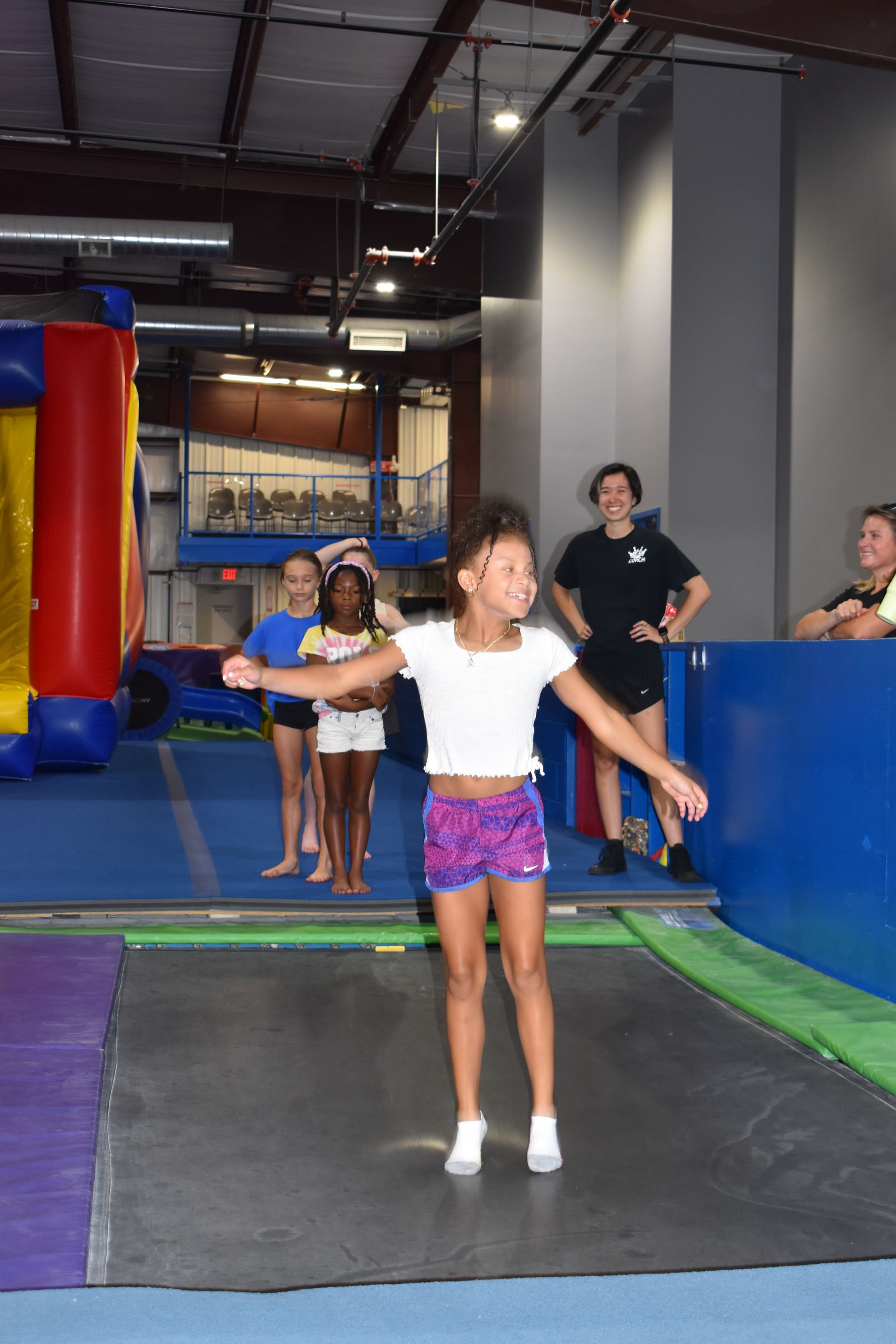 A young girl is standing on a trampoline in a gym.