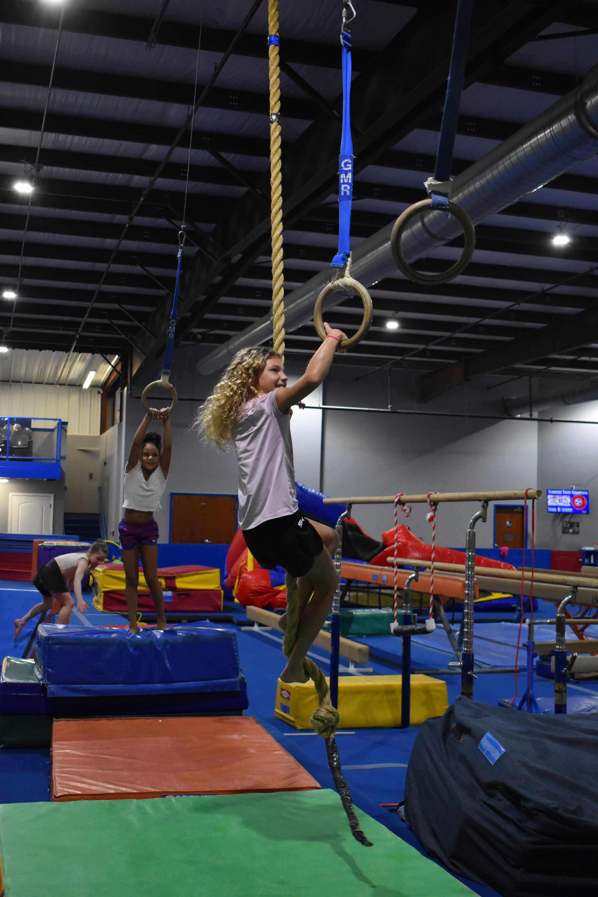 A young girl is climbing a rope ring in a gym.