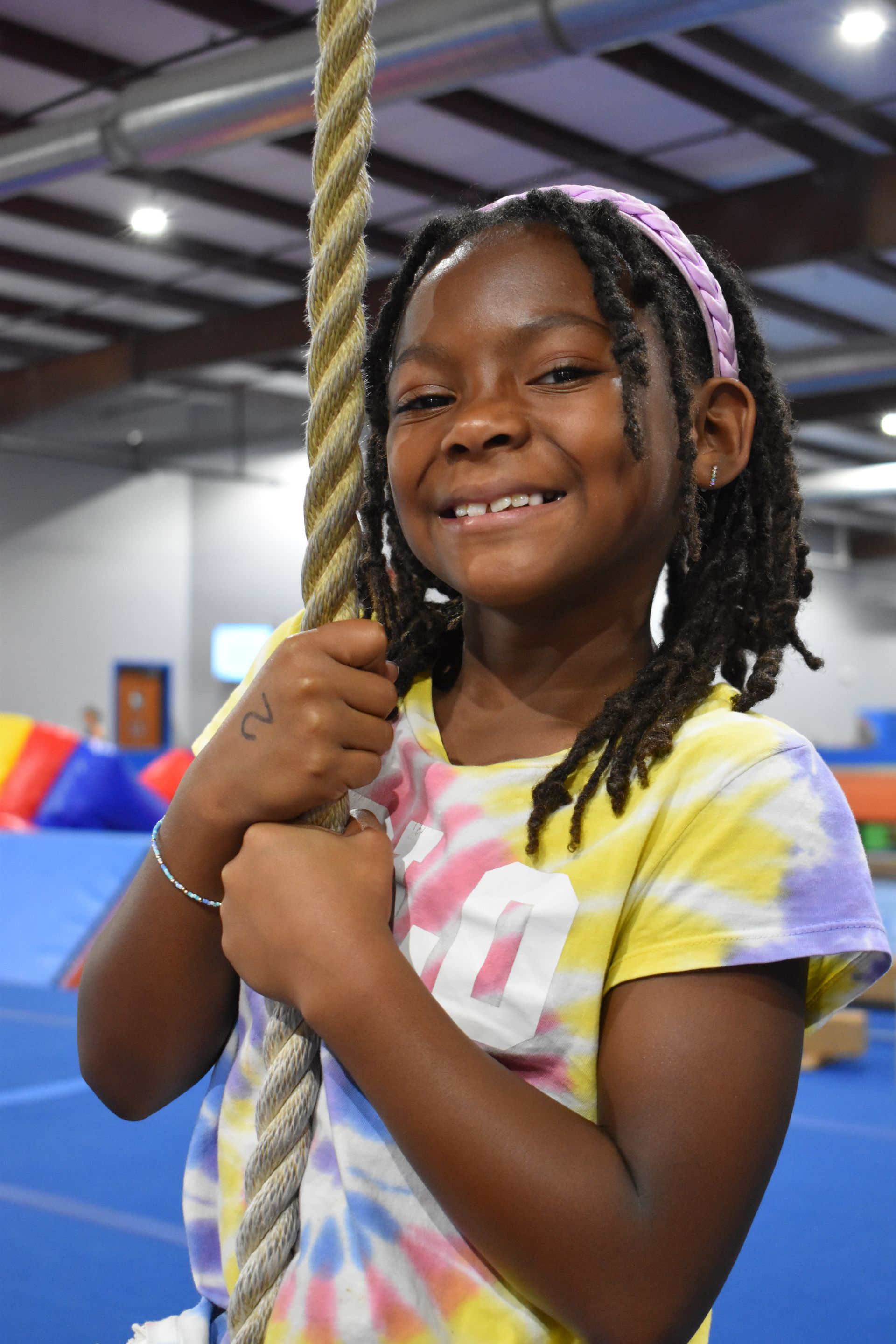 A young girl is smiling while holding a rope in a gym.