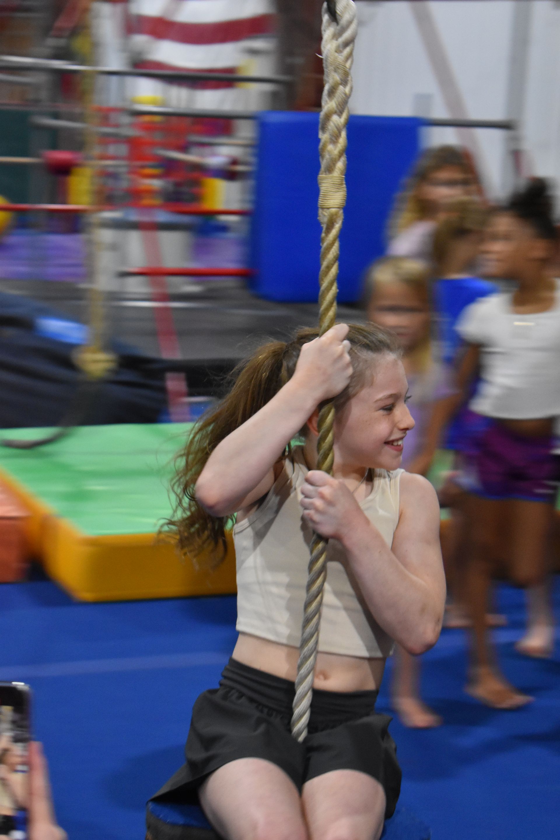 A young girl is sitting on a rope swing in a gym.