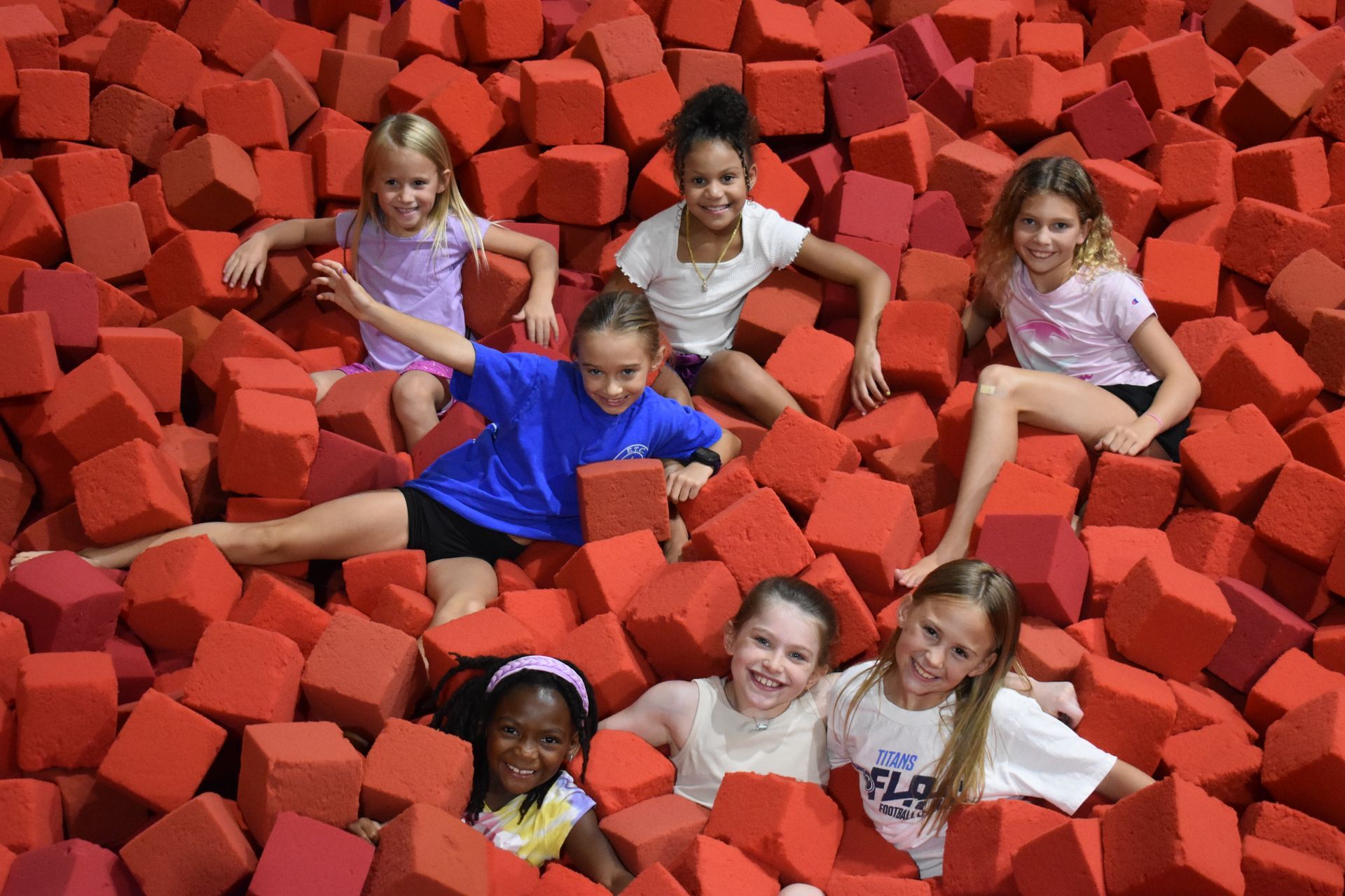 A group of young girls are sitting in a pile of red foam cubes.