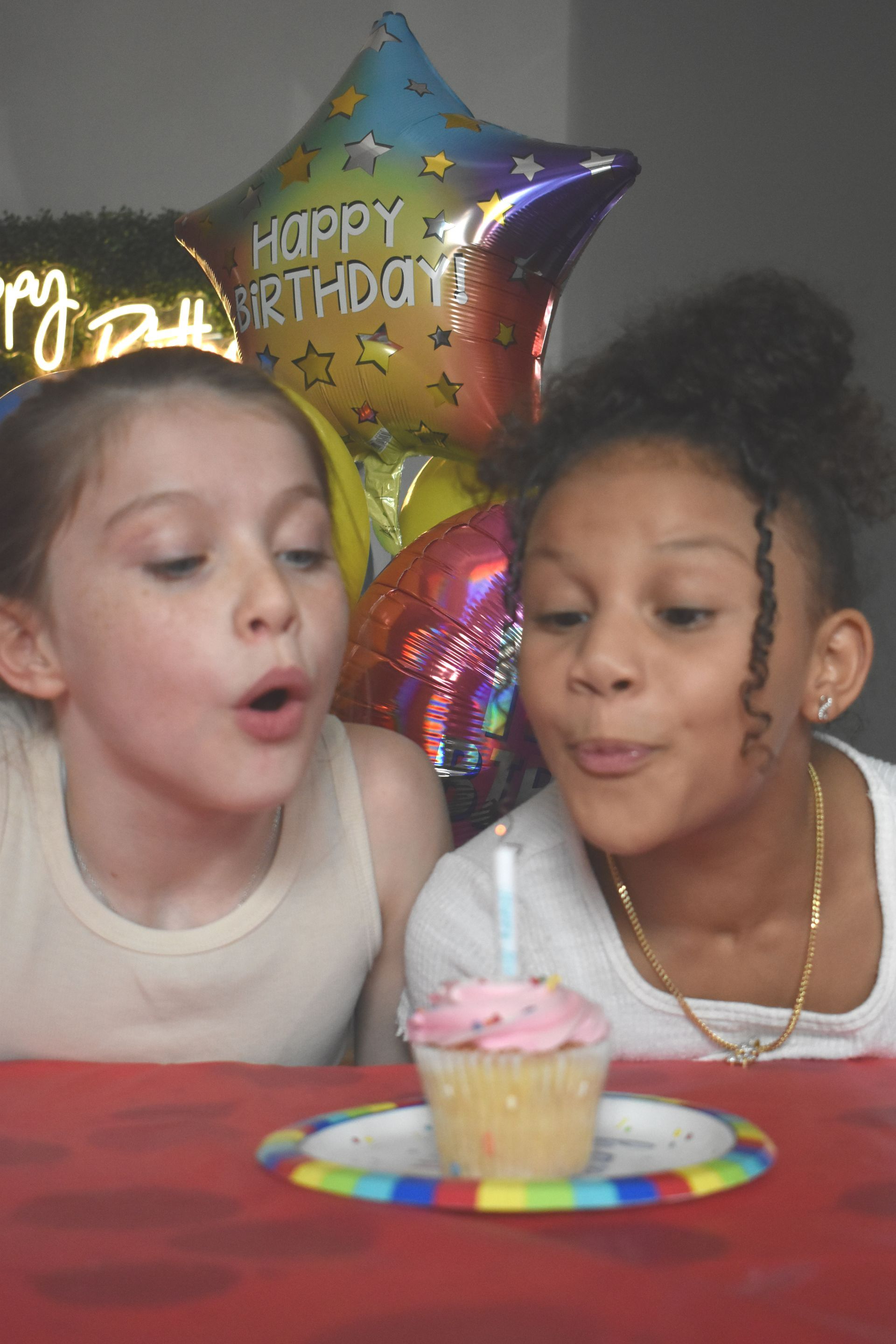 Two young girls are blowing out a candle on a cupcake at a birthday party.