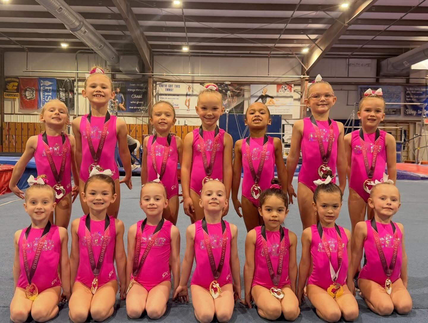A group of young girls are sitting on a balance beam in a gym.