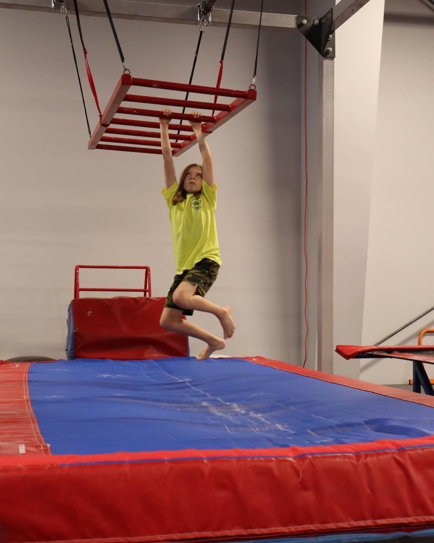 A young boy is jumping on a trampoline with a ladder hanging from the ceiling.