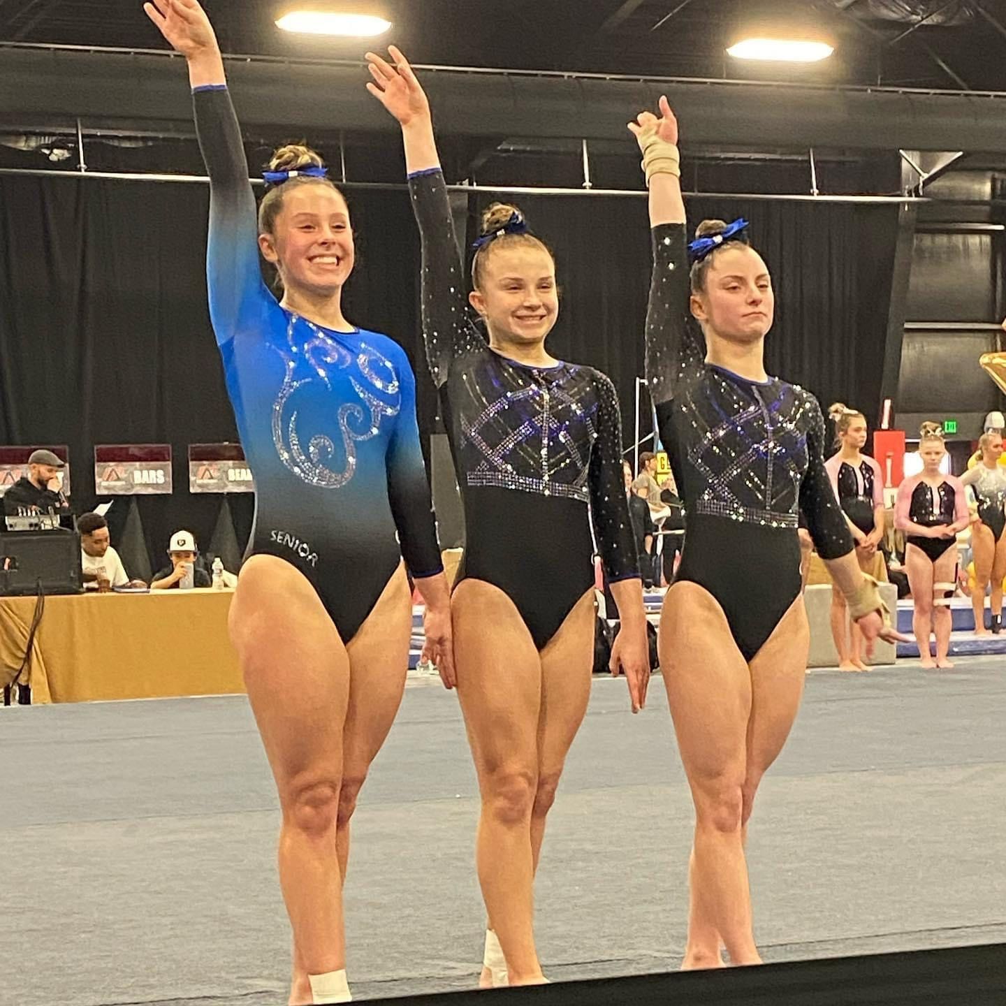 Three female gymnasts are standing next to each other with their arms in the air