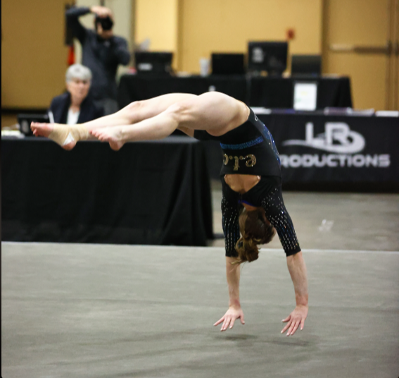 A gymnast performs a handstand in front of a lb productions sign