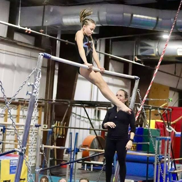 A girl is doing a split on a parallel bars in a gym