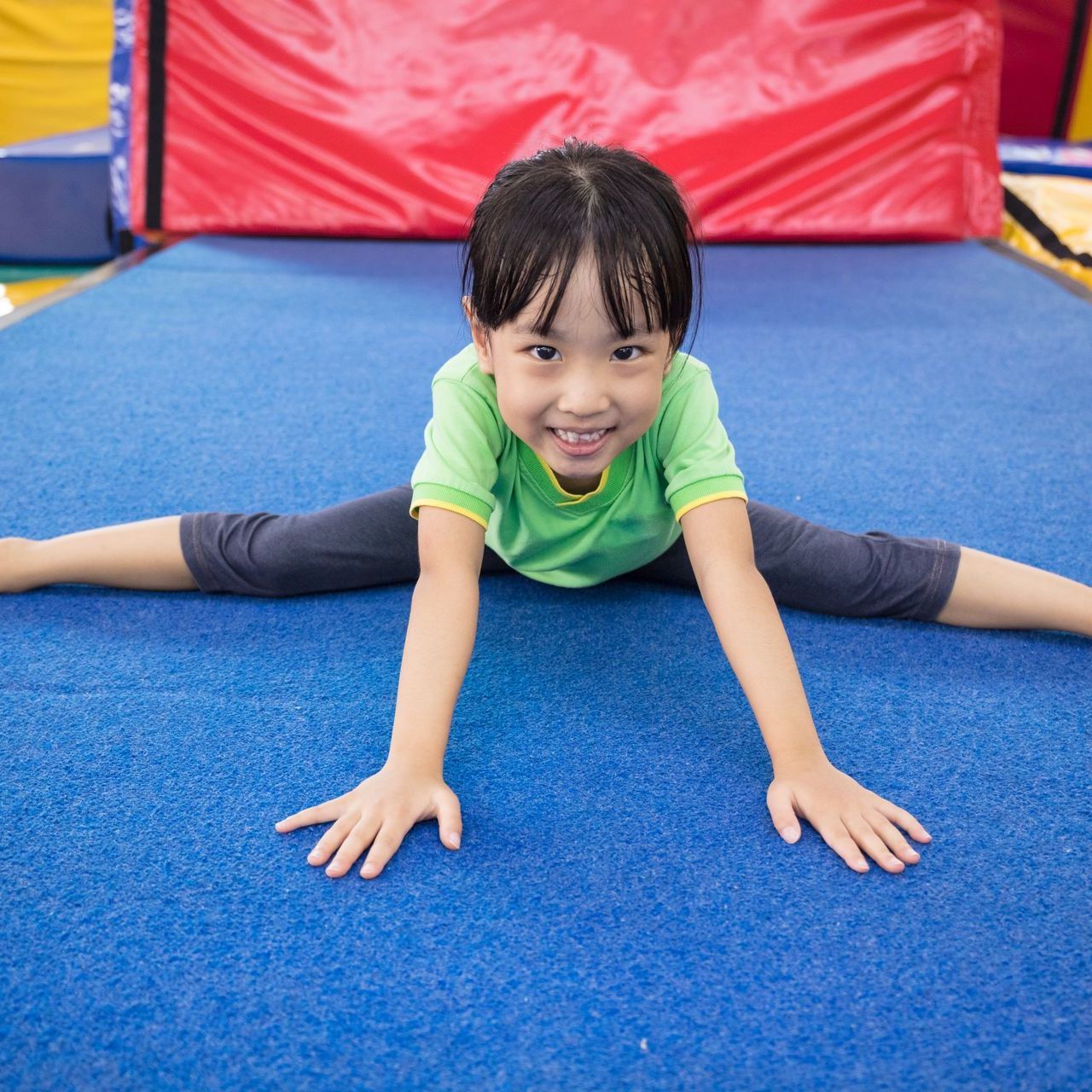 A little girl is doing a split on a blue mat