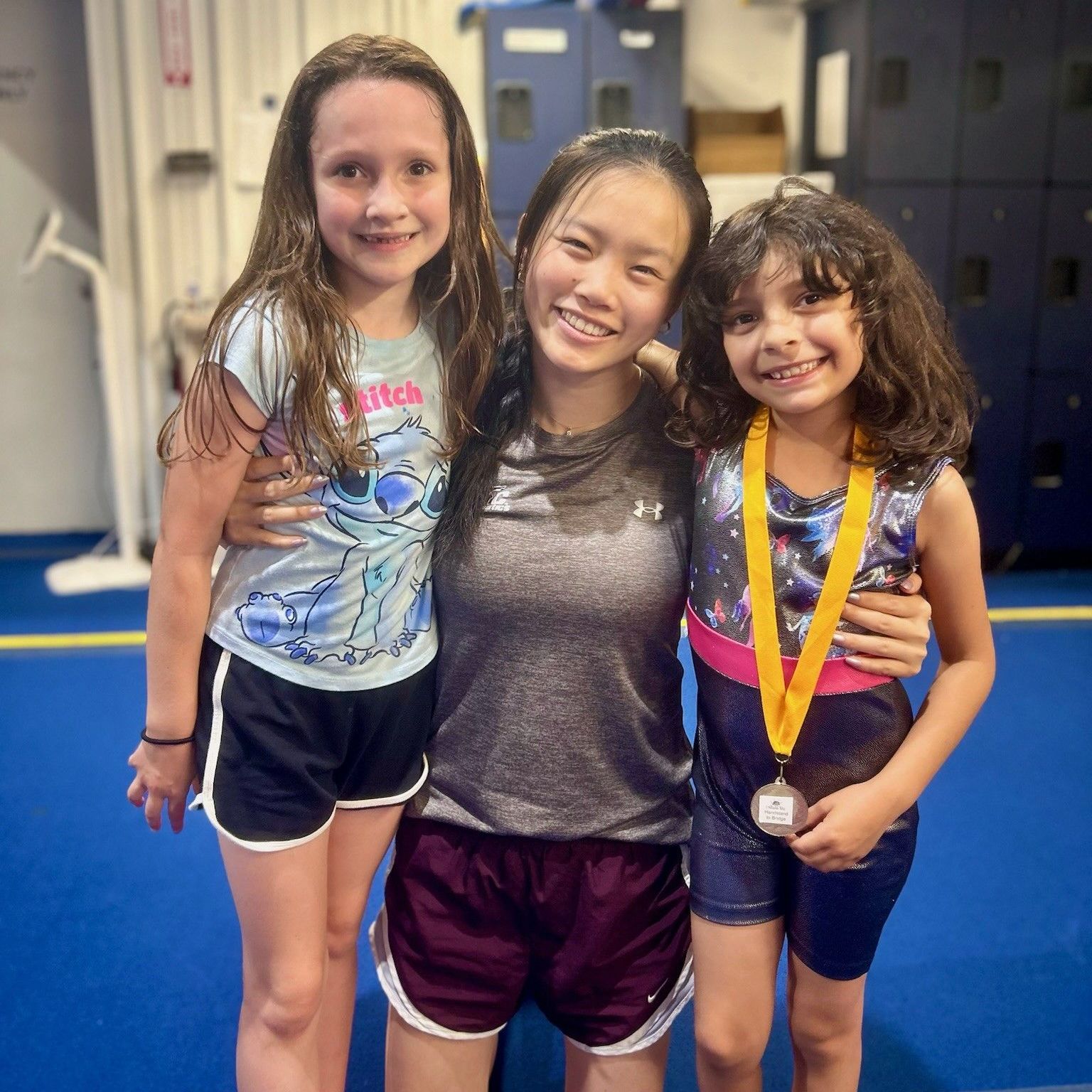 Three young girls are posing for a picture and one has a medal around her neck