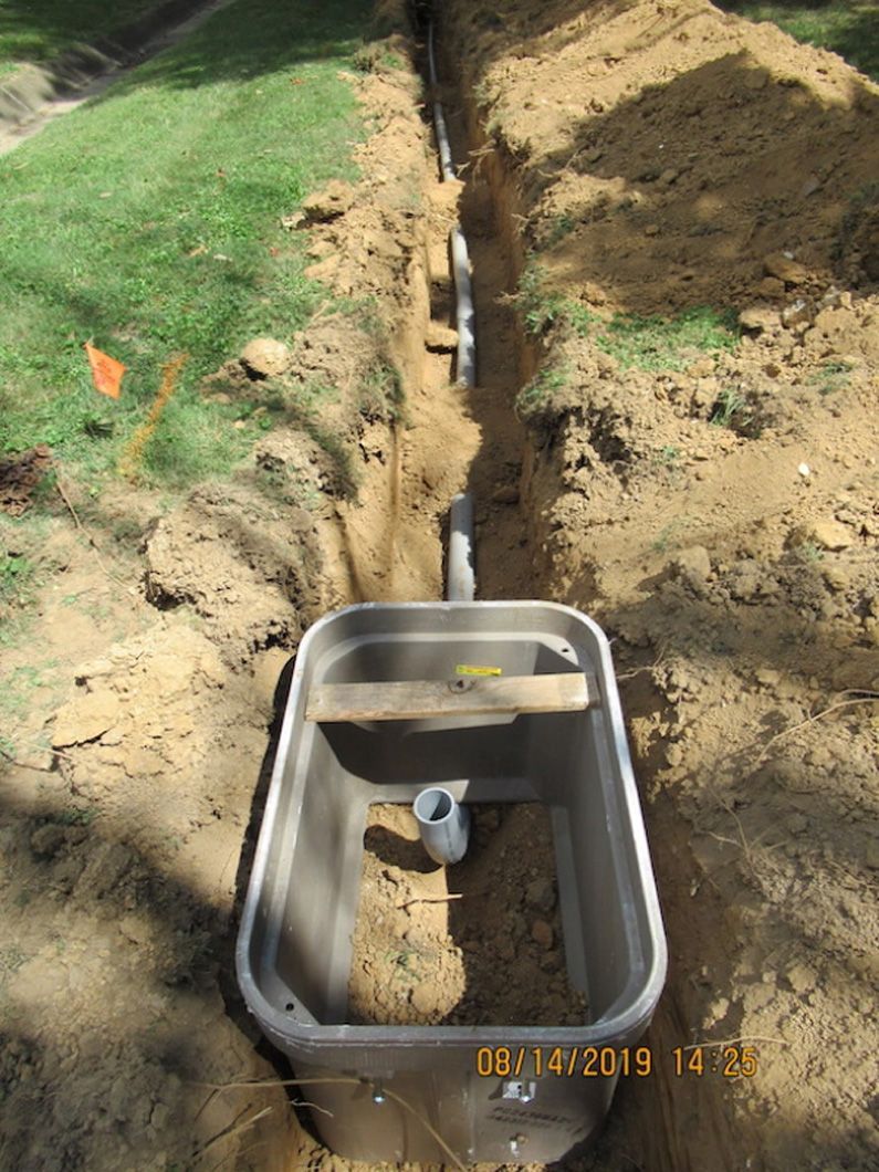 A box is sitting in the dirt next to a pipe.