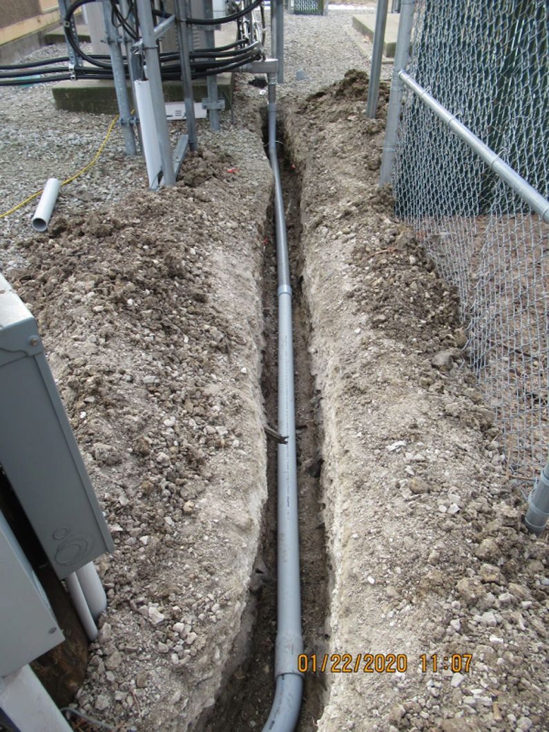 A pipe is being installed in the dirt next to a chain link fence.