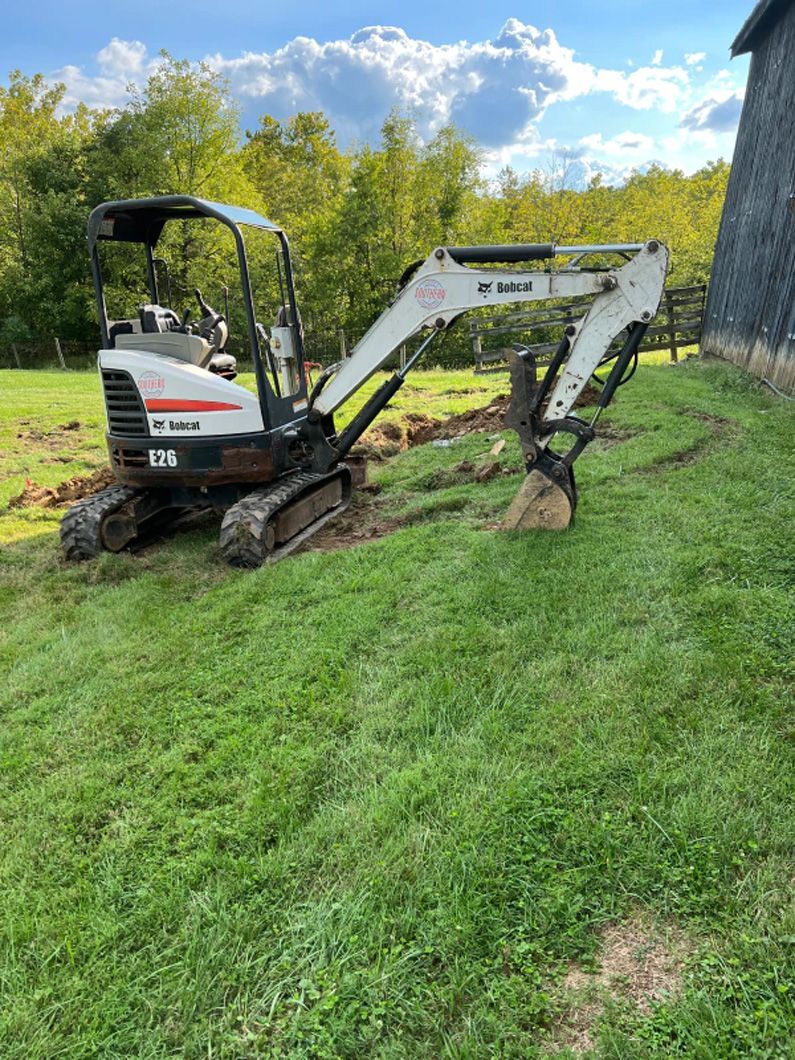 A small excavator is sitting on top of a lush green field.