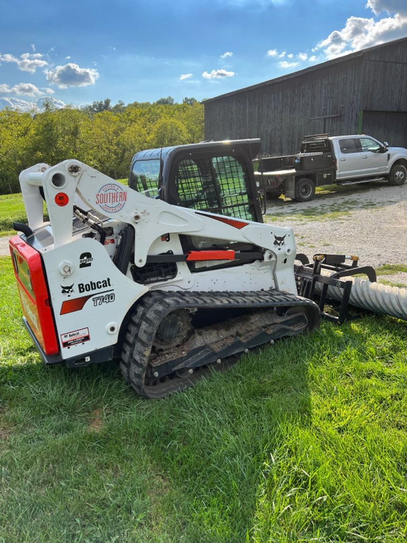 A bobcat is parked in a grassy field next to a truck.