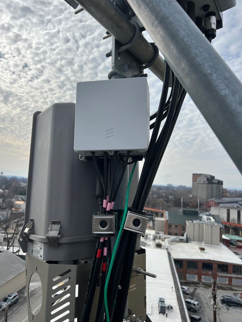 A gray box is attached to a metal pole on top of a building.