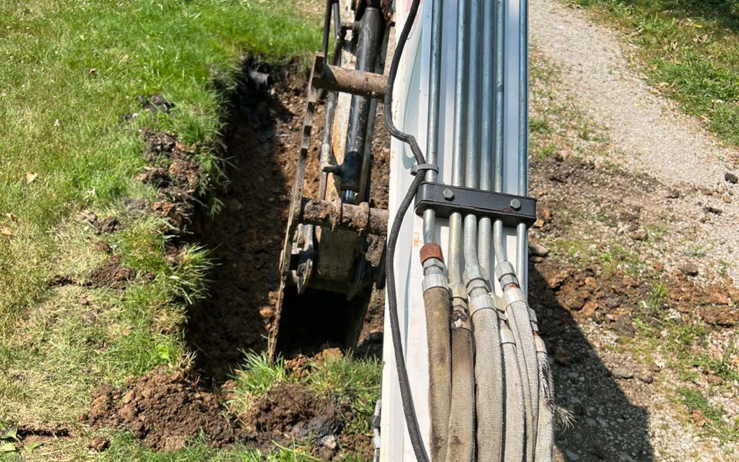 A bunch of pipes are sitting in the dirt next to a fence.