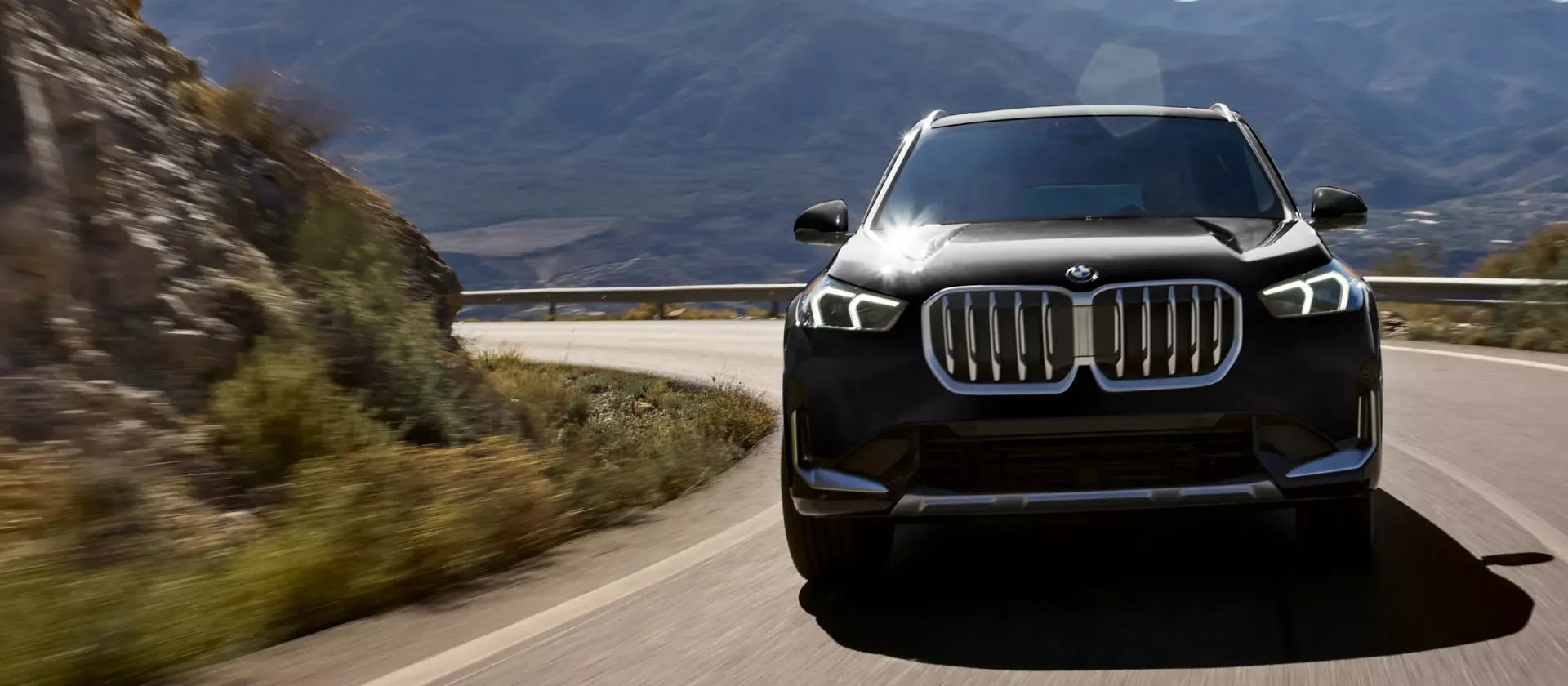 A black BMW SUV driving on a mountain road with a mountainous backdrop.