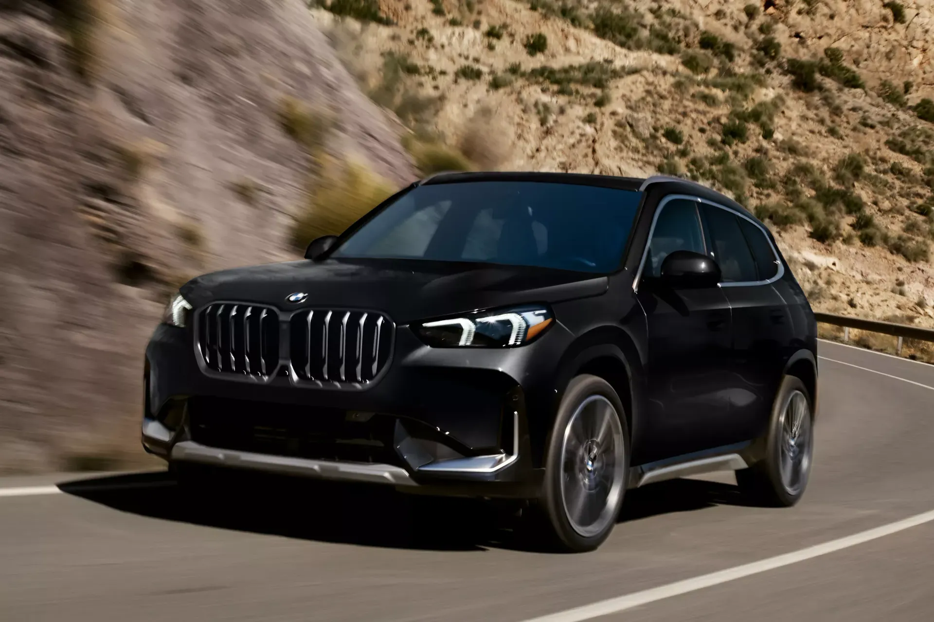 Black BMW SUV driving on a winding road with a mountainous backdrop.