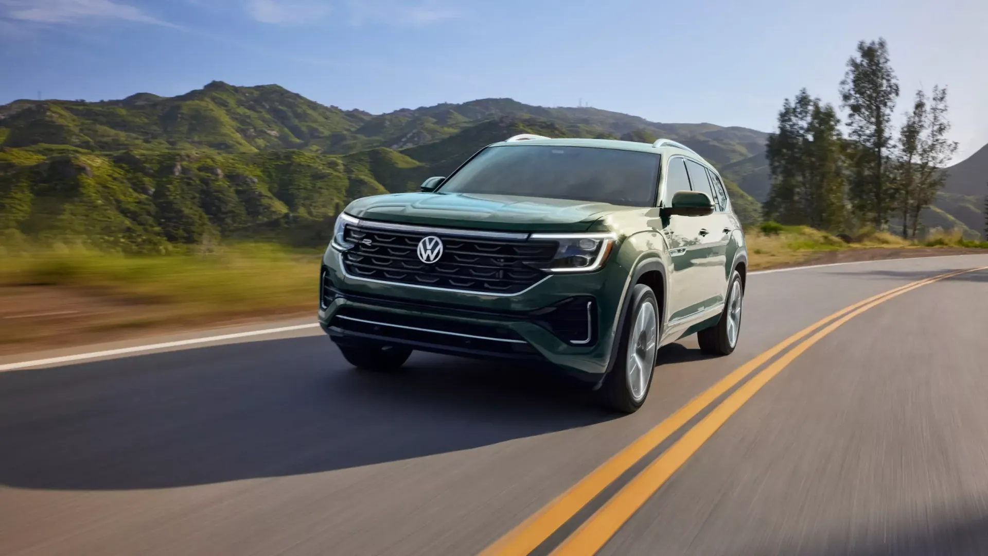 Green Volkswagen Atlas SUV driving on a winding road with a mountainous backdrop.