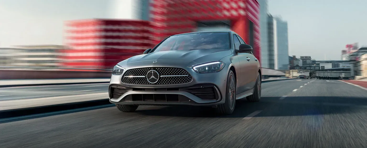 A gray Mercedes-Benz coupe on a road with blurred red building in background.
