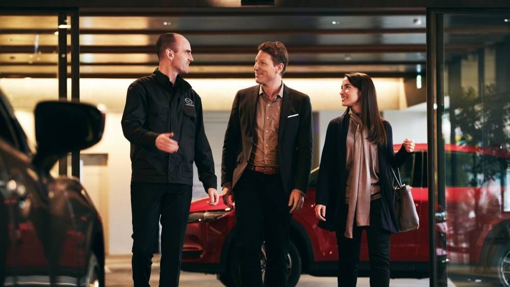 A valet greets a couple at a hotel entrance, near a red SUV.