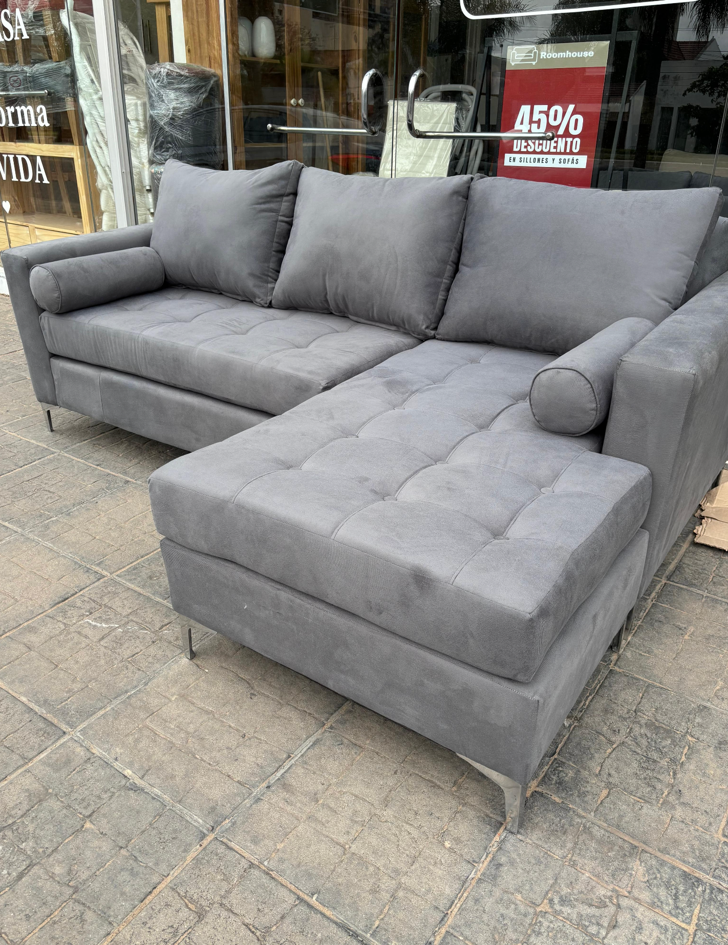 Un sofá seccional gris está sentado en una acera frente a una tienda.