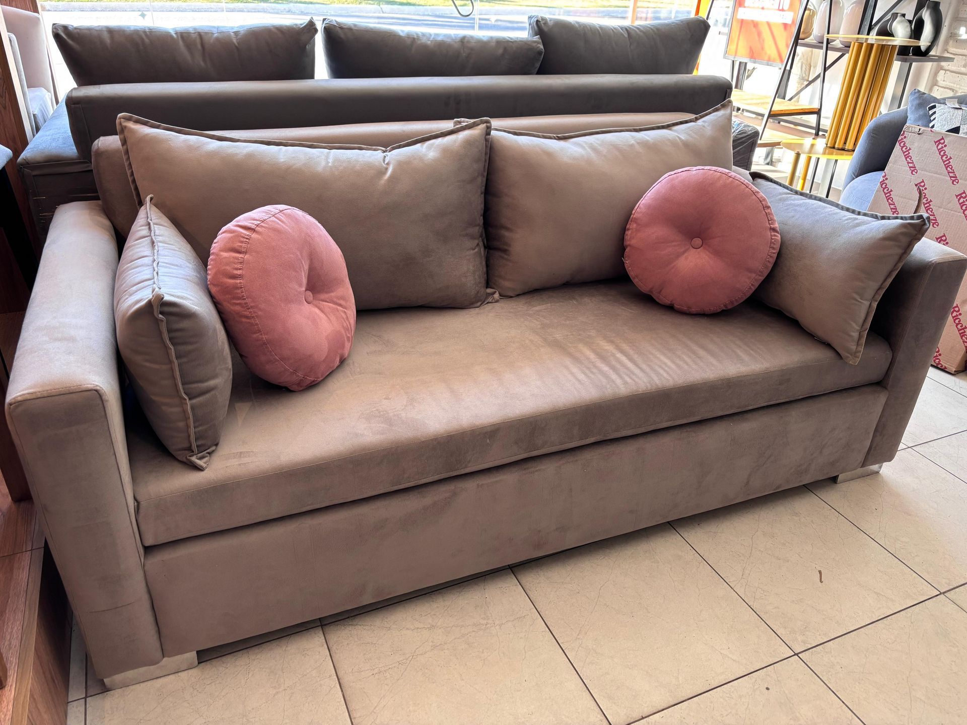 Un sofá con almohadas rosas está sobre un suelo de baldosas.