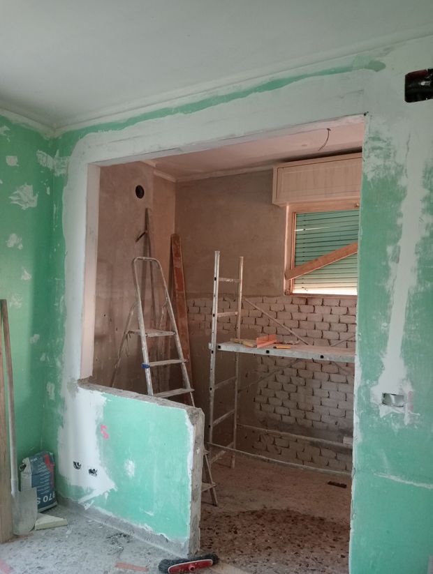 Un'impalcatura accanto a un edificio in mattoni con finiture decorative in cemento. Due secchi sono appoggiati sulla piattaforma.