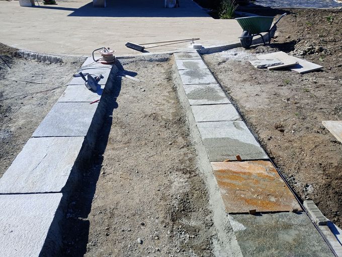 Due bassi muri in pietra in costruzione, in un ambiente di terra e ghiaia, con attrezzi nelle vicinanze.