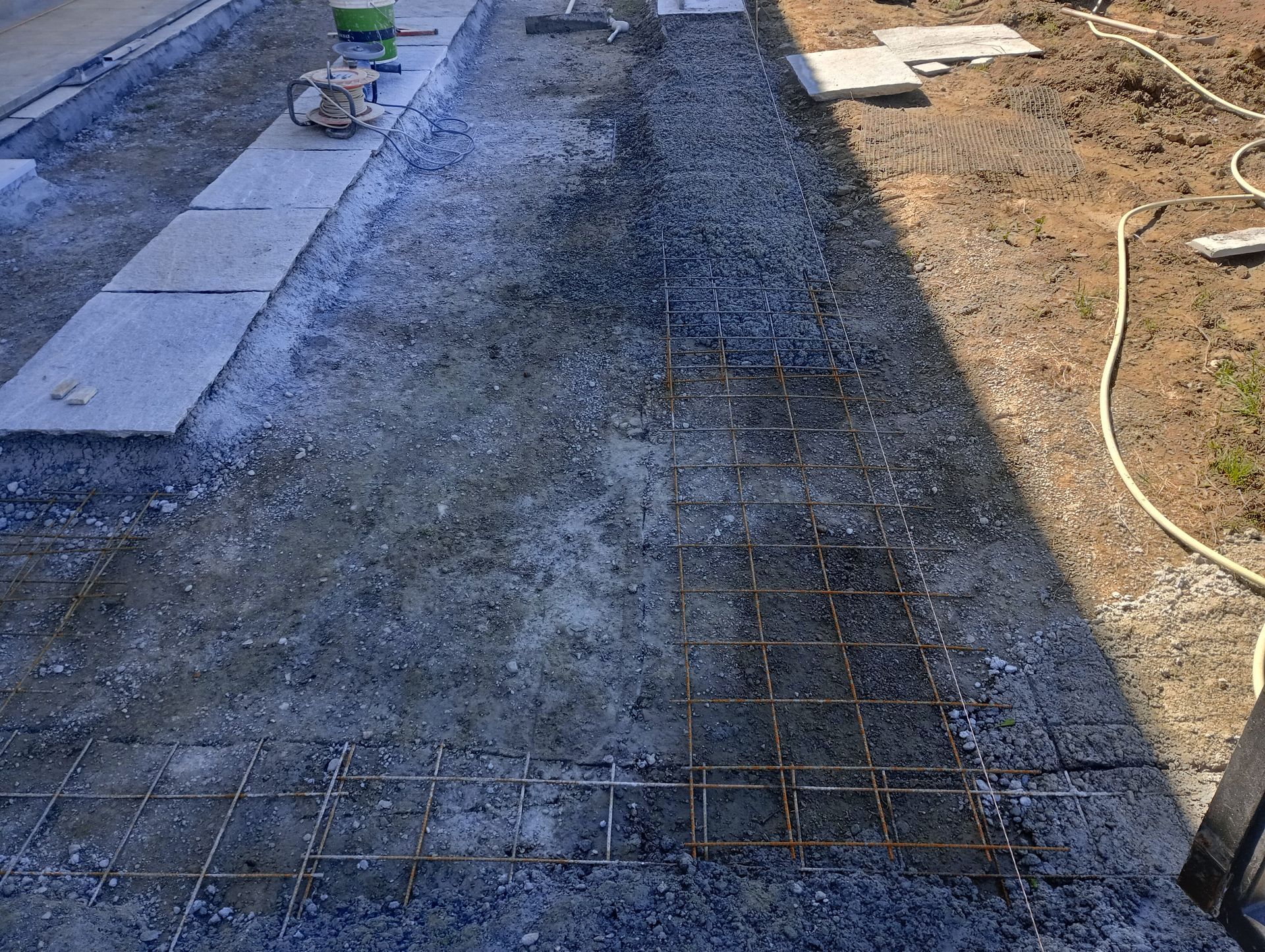 Cantiere con ghiaia, grigliato di tondini di ferro e autobloccanti, in preparazione per la pavimentazione.
