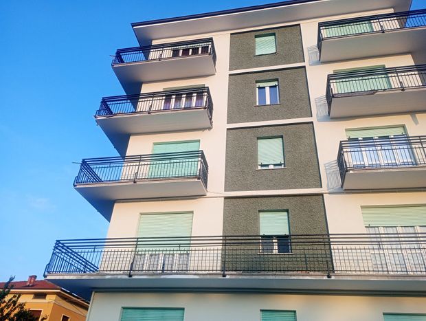 Edificio residenziale a più piani con balconi, dettagli blu e cielo azzurro.
